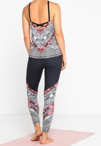 Sportieve, straps top met geometrische patronen in zwart, grijs en rood. Hooggeprijsde, aansluitende leggings met bijpassende patronen, gladde textuur.