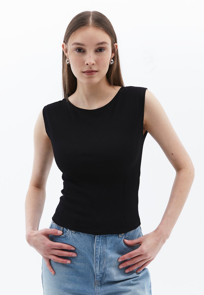 Svart ärmlös topp med ribbad textur, rundad halsringning, figurnära design och mjukt tyg, kombinerad med ljusblå denim.