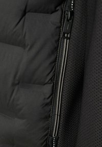 Nærbillede af en sort jakke lynlås med tekstureret stof til højre og polstret quiltet materiale til venstre.