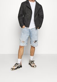 Chaqueta biker de piel sintética negra, camiseta blanca, shorts de mezclilla desgastados en azul claro, zapatillas coloridas con detalles en negro, naranja y blanco.