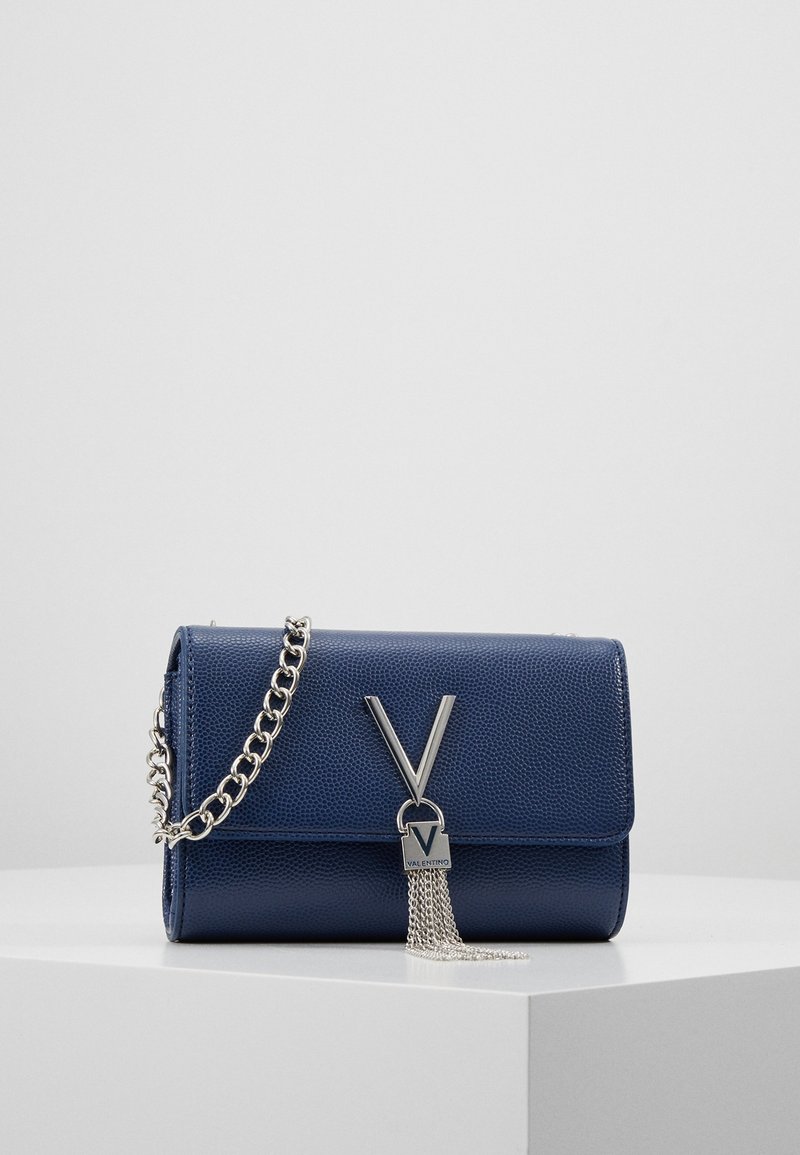 Sac à main en cuir marine avec une bandoulière en chaîne métallique, présentant un logo argenté et des franges. Forme rectangulaire avec une surface texturée.