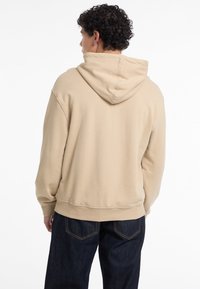 Felpa con cappuccio beige in cotone, caratterizzata da una vestibilità rilassata, tasca a marsupio e cuciture texturizzate lungo l'orlo e i polsini.