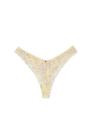 Gele kanten string met een klein roze en witte bloemenpatroon en gegolfde randen, platgelegd op een witte achtergrond.