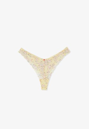 Tanga amarilla de encaje con pequeño patrón floral en rosa y blanco y bordes en forma de ondas, dispuesta sobre un fondo blanco.