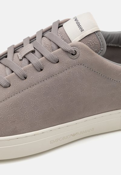 Sneakers grigi con una superficie testurizzata che presenta un sottile motivo a logo. Lacci rotondi e suola in gomma bianca con branding in rilievo.