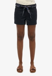 Pantaloni corta in cotone blu navy con cintura annodata a motivo paisley, caratterizzati da una vestibilità classica e orlo arrotolato. Indossati con sandali a molla marroni.