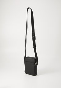 Černá crossbody taška vyrobená z texturovaného syntetického materiálu, se zipovým víkem, nastavitelným popruhem a přední kapsou s embosovaným logem.