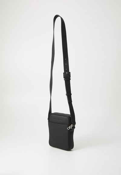 Sac bandoulière noir en matériau synthétique texturé, doté d'un dessus zippé, d'une bandoulière ajustable et d'une poche avant avec un logo en relief.