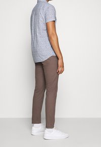 Kortärmad skjorta i blått med vitt blommönster, som matchas med bruna byxor. Modellen bär vita sneakers. Sidovy som visar passformen.