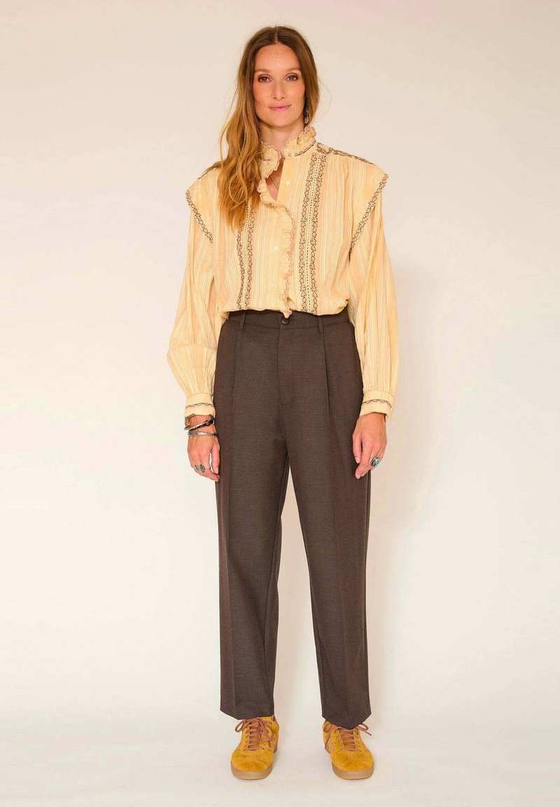 Blouse légère jaune à volants avec des rayures verticales et des accents brodés, associée à un pantalon taille haute marron foncé et des chaussures en daim jaune.
