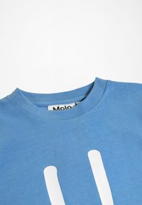 Modra bombažna majica s krožnim izrezom. V središču se nahaja velika bela grafika. Teksturna tkanina z rebrastim detajlom ovratnika.