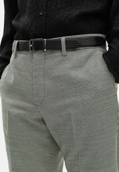 Pantaloni a motivo houndstooth in bianco e nero, realizzati in tessuto texturizzato, presentano una cintura nera con fibbia rettangolare.