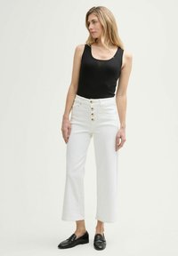 Jeans bianchi a gamba larga con vita alta, caratterizzati da una chiusura a cinque bottoni, abbinati a un top aderente nero. Mocassini neri completano l'outfit.