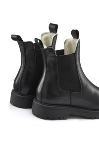 Schwarze Lederstiefeletten mit dicken Gummisohlen, elastischen Seitenpaneelen, Zuglaschen und weißem Fleecefutter, das innen sichtbar ist.