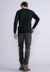Maglione nero testurizzato con maniche lunghe e dettagli a coste, abbinato a Jeans grigi e stivali marroni, visto da dietro.