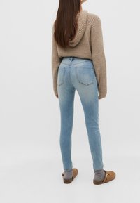 Light blue skinny jeans with a high waist, featuring back pockets and a subtle faded texture, paired with a brown knitted hoodie and clogs.