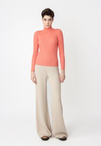 Koralle gerippter Rollkragenpullover mit langen Ärmeln, kombiniert mit weit geschnittenen beige Hosen, die eine sanfte Textur und eine lockere Passform bieten.