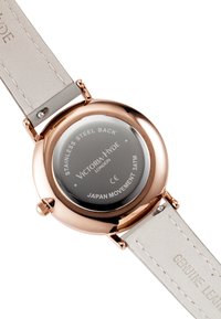 Montre ronde avec un boîtier en acier inoxydable rose doré, un fond en verre gris et un bracelet en cuir véritable gris clair avec des détails de couture.