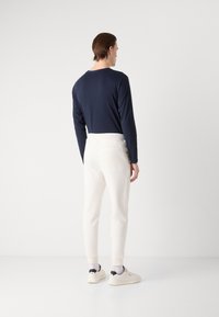 Camisa de manga larga azul marino con un escote redondeado, combinada con joggers crema que tienen un bolsillo y puños de canalé. Zapatillas blancas con detalles en negro.