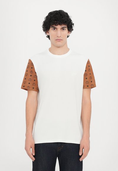 Witte t-shirt met bruine, gepatterneerde mouwen met diamanten en logo's. Zacht materiaal, ronde halslijn en een relaxte pasvorm. Blauwe jeans complementeren het ontwerp.