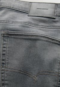 Jeansi din denim gri cu o suprafață texturată, având o etichetă din piele la talie și cusături decorative pe buzunare.