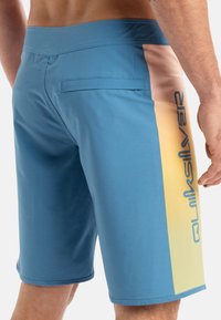 Modré plavecké šortky s pastelovou gradientnou bočnou panelou a logom Quiksilver. Vyrobené z hladkého, ľahkého materiálu s zadnou kapsou.