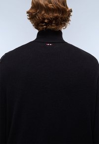 Sort strikket sweater med høj krave, der har en subtil rød og hvid detalje ved bagekanten af kraven. Glat tekstur, afslappet pasform.