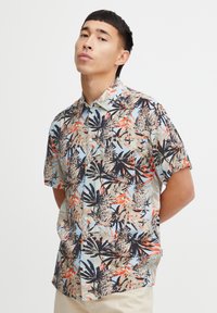 Tričko s krátkym rukávom vyrobené z ľahkého materiálu so vzorom v tropickej tematike, na ktorom sú ananásy a palmové listy na svetlom pozadí.
