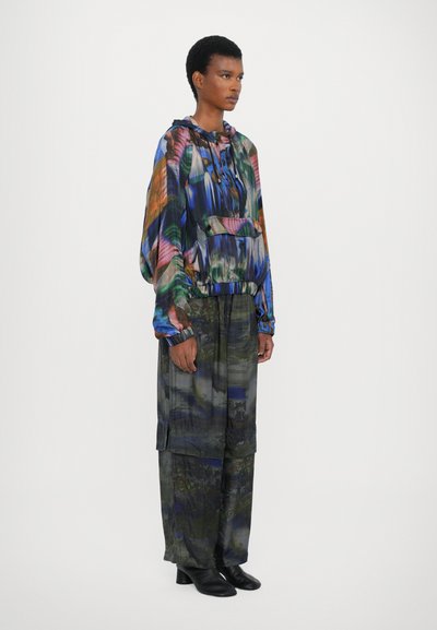 Farverig, mønstret hættebluse med snor, parret med løse, mørke, teksturerede bukser. Sorte ankelstøvler fuldender outfittet.