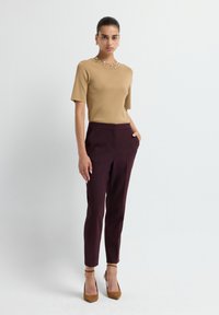 Top court à manches courtes avec des accents de perles décoratives, associé à un pantalon ajusté bordeaux et des chaussures à talons beiges, sur fond neutre.