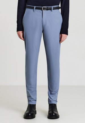 Helle blaue Hosen aus einem glatten Stoff, mit schlanker Passform, Gürtelschlaufen und einem schwarzen Gürtel. Getragen mit schwarzen Stiefeletten.