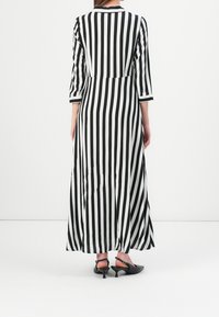 Robe longue rayée noir et blanc avec manches trois-quarts, corsage ajusté et jupe évasée, associée à des escarpins noirs à bride arrière.