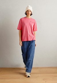 Rosa bomullsgenser med korte ermer og frontlomme, kombinert med løse blå denimbukser. Brukt med en hvit strikket lue og sneakers.