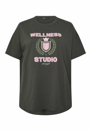 Dunkelgrünes, übergroßes T-Shirt mit pinkem Schriftzug "WELLNESS STUDIO est. 1998" und einem Lorbeerkranz- und Schild-Emblem in der Mitte.