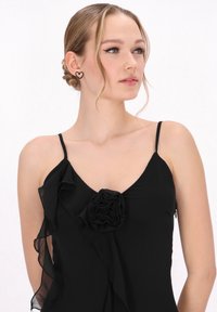 Fekete ruha spagetti pántokkal, fodros szélekkel és középső virágmintával. Simaságán rétegezett textúra. Szív alakú fülbevalók.