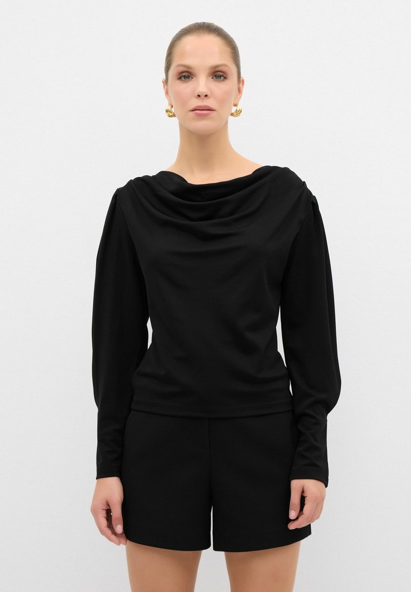 Schwarzes Langarmoberteil mit drapierter Ausschnittlinie, glatter Textur und figurbetontem Schnitt, kombiniert mit schwarzen Shorts. Schlichtes, stimmiges Design.