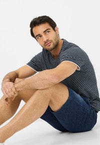 T-shirt a righe navy e bianche con maniche corte, abbinato a pantaloni corti in denim scuro. Il tessuto appare morbido con una vestibilità casual.