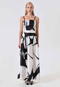 Robe maxi noire et blanche, présentant un imprimé abstrait, un décolleté carré, des fines bretelles et un tissu fluide avec une texture lisse.