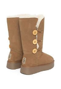 Botas de ante marrón hasta la pantorrilla con forro de pelo sintético, que cuentan con tres botones de madera decorativos y una suela de goma plana para mayor tracción.