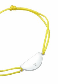 Charm en métal argenté en forme de demi-lune sur un bracelet en cordon tressé jaune, avec une finition polie et des gravures sur le charm.