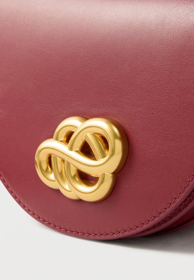 Στρογγυλή τσάντα χειρός από βυσσινί δέρμα με κούμπωμα σε σχήμα χρυσού κόμπου. Λείο υλικό με αντιθετικό ράψιμο κατά μήκος των άκρων.