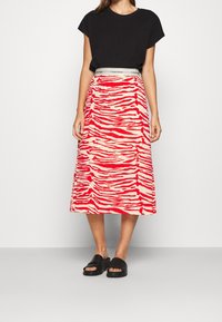 Svart kortärmad topp med en röd och krämfärgad zebra-randig midikjol, som har en Calvin Klein-logotyp på midjebandet. Matchad med svarta slidesandaletter.