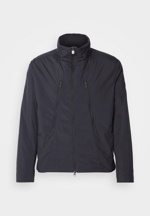 Črna lahka jakna z visokim ovratnikom, dvema sprednjima žepoma na zadrgo in gladkim, rahlo teksturiranim materialom. Zadrga na sprednji strani.