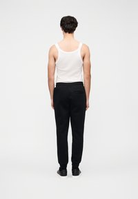 Λευκό αμάνικο τοπ και μαύρη φόρμα, με ελαστική μέση, ρεβέρ στα τελειώματα και πίσω τσέπη. Φορεμένα με μαύρα αθλητικά παπούτσια.