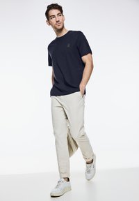 Námořnické tričko s kulatým výstřihem a decentním logem, v kombinaci se světle béžovými kalhotami rovného střihu a bílými nízkými teniskami. Čistý, ležérní vzhled.