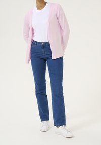 Cárdigan rosa claro, camiseta blanca, jeans azules y zapatillas blancas. El cárdigan tiene un diseño de apertura frontal; los jeans son ajustados con un corte recto.