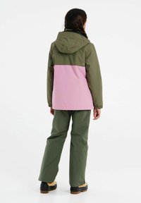 Groene en roze kleurgeblokkeerde waterdichte jas met een capuchon, voorzien van elastische manchetbanden en bijpassende groene broek en zwarte laarzen.