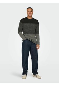 Suéter de manga larga para hombre en gris degradado, con una parte superior oscura que se va transformando en tonos más claros, con punto texturizado y escote redondo. Combinado con jeans oscuros.