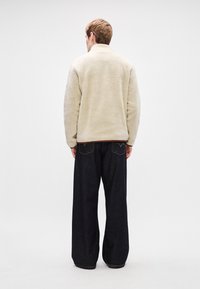 Creme fleecejakke med høj krave, almindelig pasform og tekstureret stof, kombineret med mørke brede denimbukser.