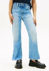 Jeans a palazzo di colore blu chiaro in denim, con vita alta, cinque tasche e una leggera scoloritura. Mocassini neri con dettaglio a fibbia.